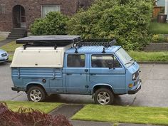 an old blue van parked in front of a house with a surfboard on the roof