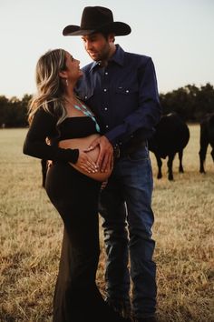 a pregnant woman standing next to a man in a cowboy hat with cows behind her