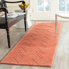 an orange rug on the floor in a living room with a chair and window behind it