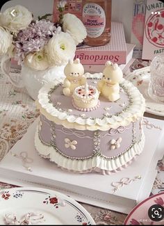 there is a cake with two teddy bears on it and some flowers in the background