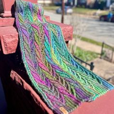 a colorful knitted blanket sitting on top of a wooden bench next to a street