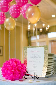 a table topped with lots of pink and gold balloons next to a card on top of a plate