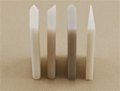 four white candles sitting on top of a table next to each other in front of a beige background