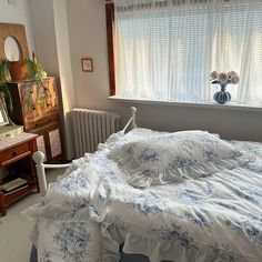 a bed with white and blue comforter in front of a window next to a dresser