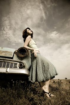 a woman leaning on the hood of an old car in a field royalty photo - free