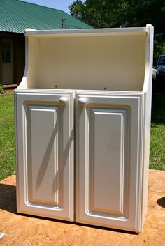 a white storage cabinet sitting on top of a wooden table in front of a house