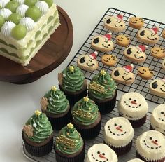 cupcakes with frosting and christmas decorations are on a cooling rack next to a cake