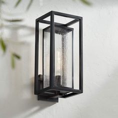 an outdoor wall light that is hanging on the side of a white wall with green leaves