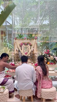 three people sitting at a table with food in front of them and flowers on the wall behind them