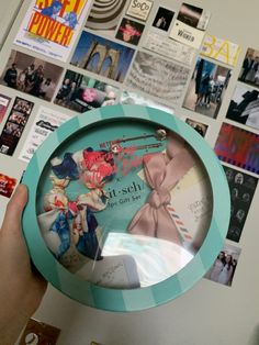 a person holding up a clock in front of a wall covered with pictures and magnets