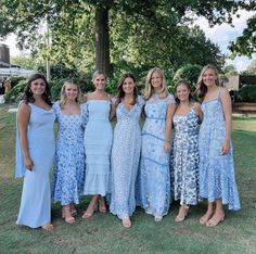 four women in dresses posing for a photo together on the lawn at an outdoor event