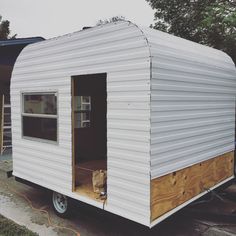 a small white trailer sitting on top of a driveway next to a tree and building