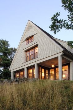 a white house sitting on top of a lush green hillside next to tall grass and trees