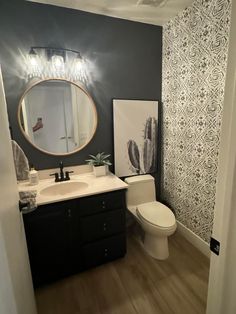 a white toilet sitting next to a bathroom sink under a round mirror on top of a wooden floor