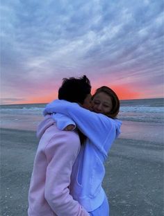 two women hugging each other on the beach at sunset or sunrise with clouds in the background