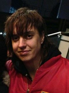 a man with long hair wearing a red jacket and holding a dog in his arms