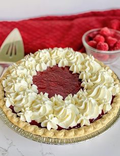 a pie with whipped cream and raspberries in the background