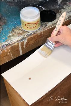 a person is using a brush to paint the top of a piece of wooden furniture