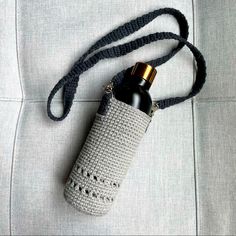 a crocheted bag with a bottle in it on top of a white couch