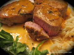 two pieces of meat with cheese and pasta on a white plate next to green leafy greens