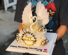 a birthday cake with white frosting and gold decorations on the top is being held by a person