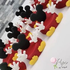 mickey mouse cake with red and yellow frosting on it's side, surrounded by black and white fondant decorations