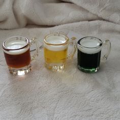 three different types of beer in glass mugs on a white blanket, one is green and the other is brown