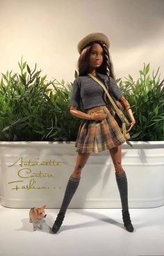 a barbie doll is standing next to a cat and planter with plants in the background