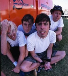 four young men sitting on the ground in front of a bus