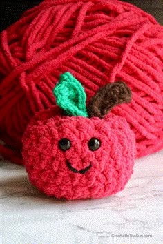 a red ball of yarn with a smiling face on it and a crocheted apple