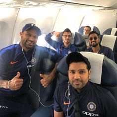 several men sitting on an airplane with headphones in their ears and one man giving the thumbs up