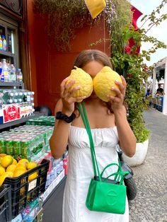 a woman holding up two lemons in front of her face while standing next to a fruit stand