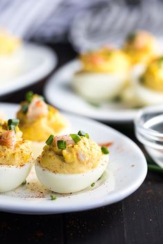 deviled eggs are topped with shrimp and garnished with scallions on a white plate