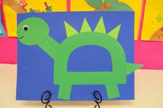 a paper cut out of a green dinosaur on a blue and pink background with black hooks