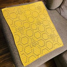 a yellow crocheted blanket sitting on top of a gray couch next to a wooden floor