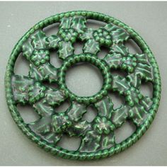 a green and white brooch with leaves on it's back side, sitting on a gray surface