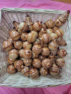 a wicker basket filled with brown and white ceramic ornaments on top of a pink table cloth