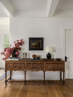 a wooden table sitting in the middle of a living room next to a painting on the wall