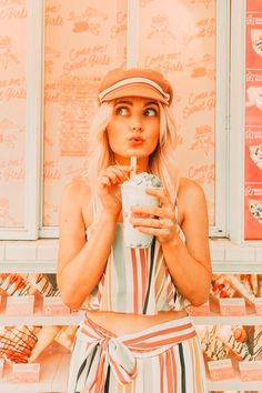 a woman holding a drink in her right hand while standing next to a wall with donuts on it