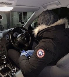 a man sitting in the driver's seat of a car wearing a coat and gloves