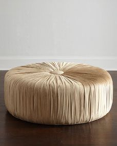 a large round ottoman sitting on top of a wooden floor next to a white wall