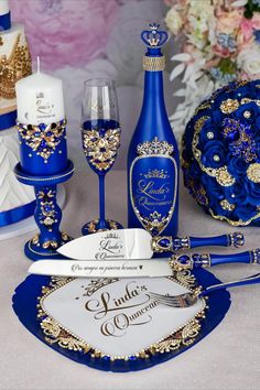 a table topped with blue and gold wedding decorations next to wine glasses, plates and candles