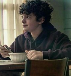 a young man sitting at a table with a cup and spoon in front of him