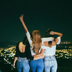 three women standing on top of a hill at night with their arms in the air