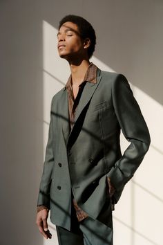 a man standing in front of a wall with his hands on his hips wearing a suit and tie