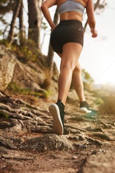 a woman running down a rocky trail in the woods with her shoes on and one leg up