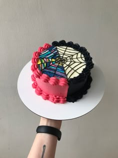 a hand holding a cake on top of a white plate with spider webs and pink frosting