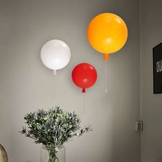 three balloons are hanging on the wall above a vase with flowers and an orange balloon