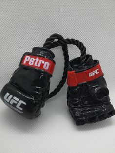 two pairs of black boxing gloves with red wrist wraps on top of each other, sitting on a white surface