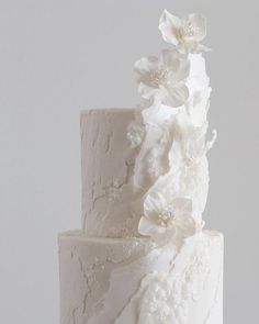 a three tiered cake with white flowers on top is sitting on a wooden stand